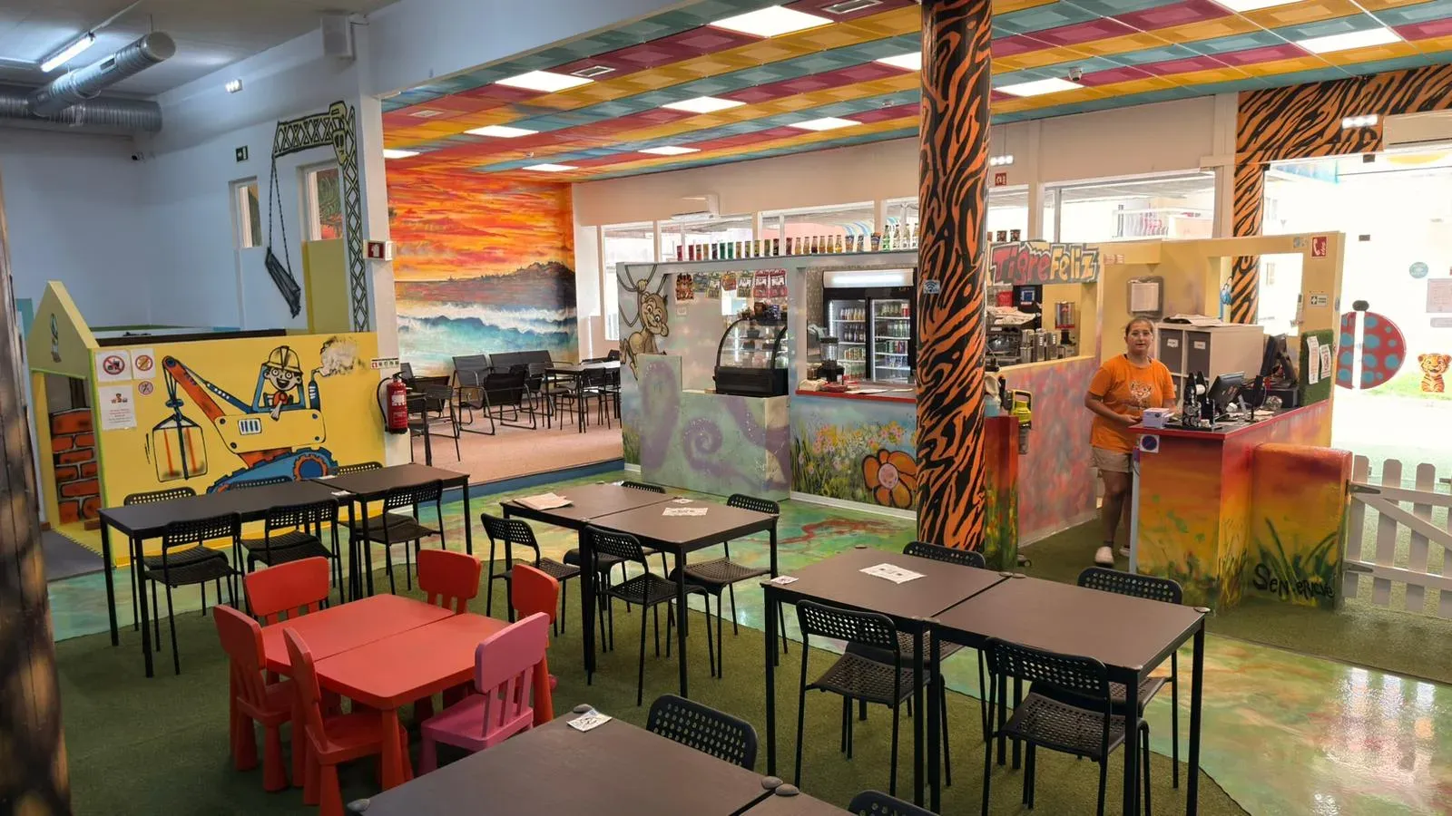 The café counter at Tigre Feliz, with coffee machine, cake display and drinks fridge, and the seating tables with children’s chairs