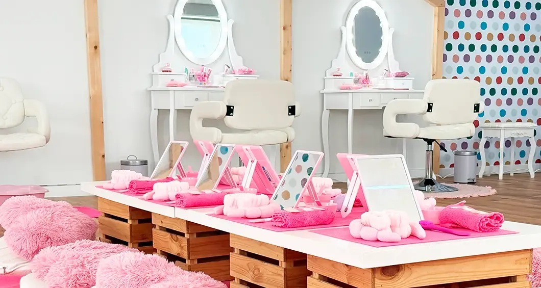 Encimera de SPA infantil con espejos iluminados, sillas blancas y toallas rosas, en Anima Park