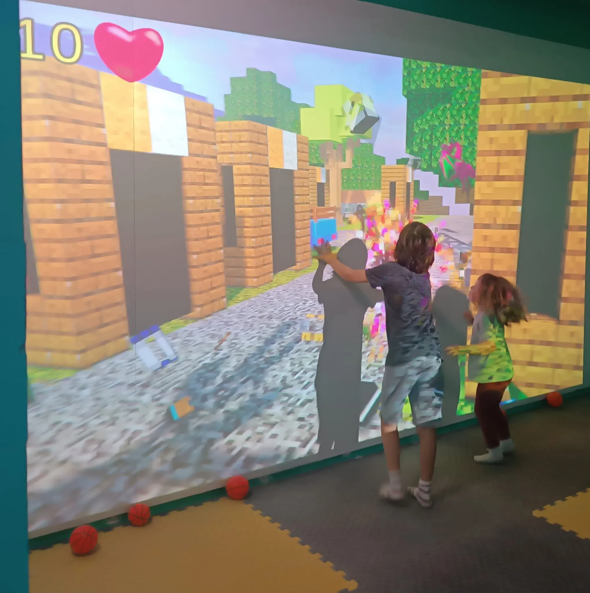Two children playing an interactive projection game on a giant wall screen